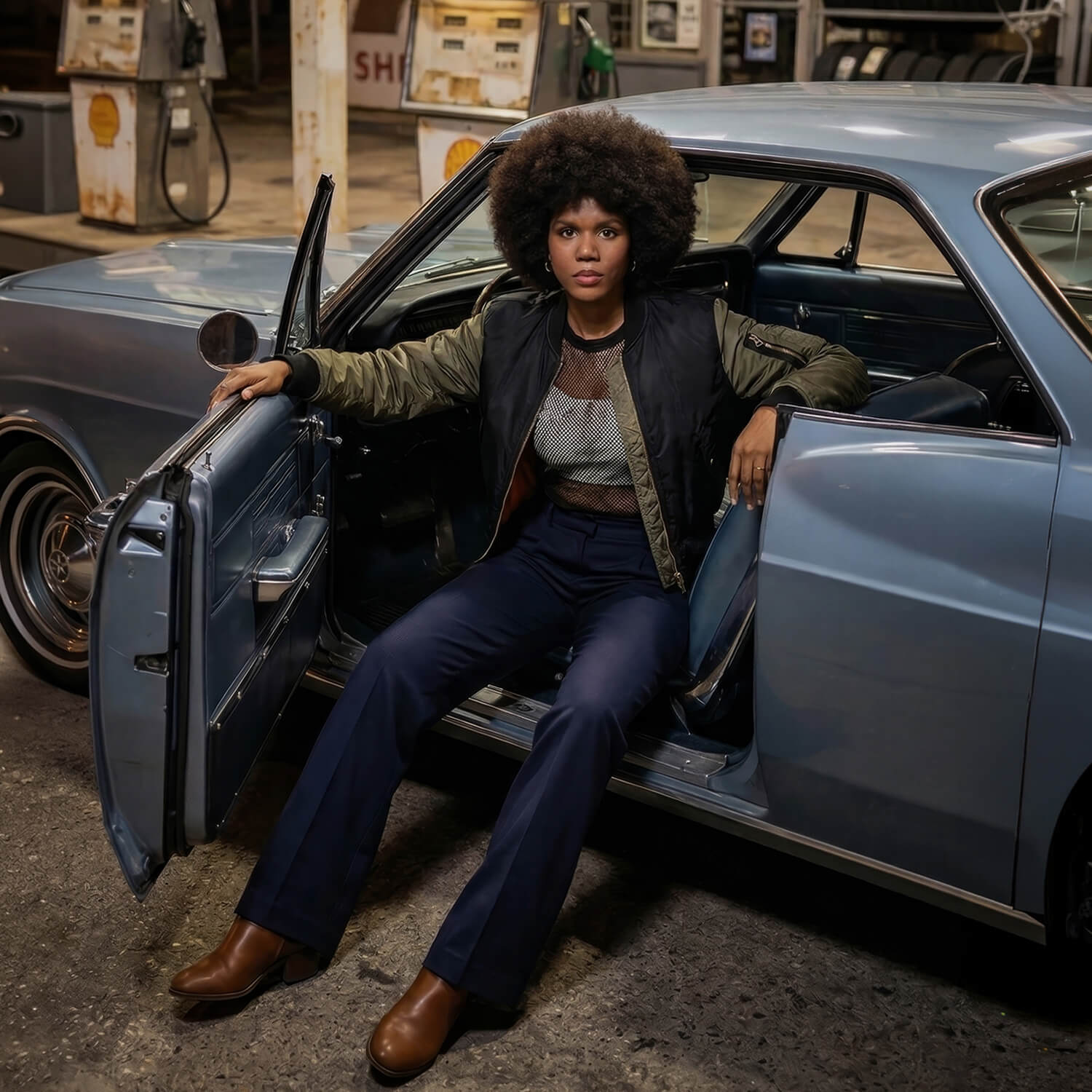 Keysha Love sitting in a classic blue car at a vintage gas station, capturing a cinematic neo-soul aesthetic.