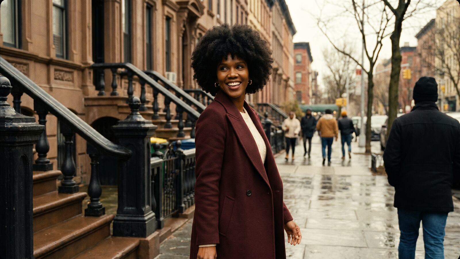 Keysha Love smiling on a Harlem brownstone street in a burgundy coat on a rainy day.